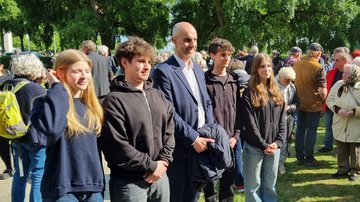 In der Mitte steht ein Mann. Links und rechts Jugenliche. Alle lächeln.