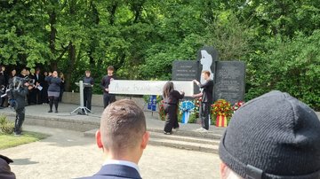 Jugendliche halten vor dem Ehrenmal ein Banner hoch. Darauf zu lesen der Name Anne Frank