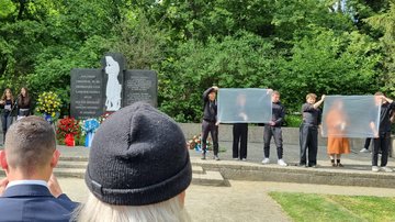 Jugendliche halten neben dem Mahnmal Folien hoch. Dahinter kann man einen Mensch erahnen
