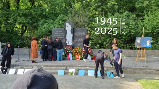 Jugendliche legen vor einem Ehrenmal Spiegel nieder